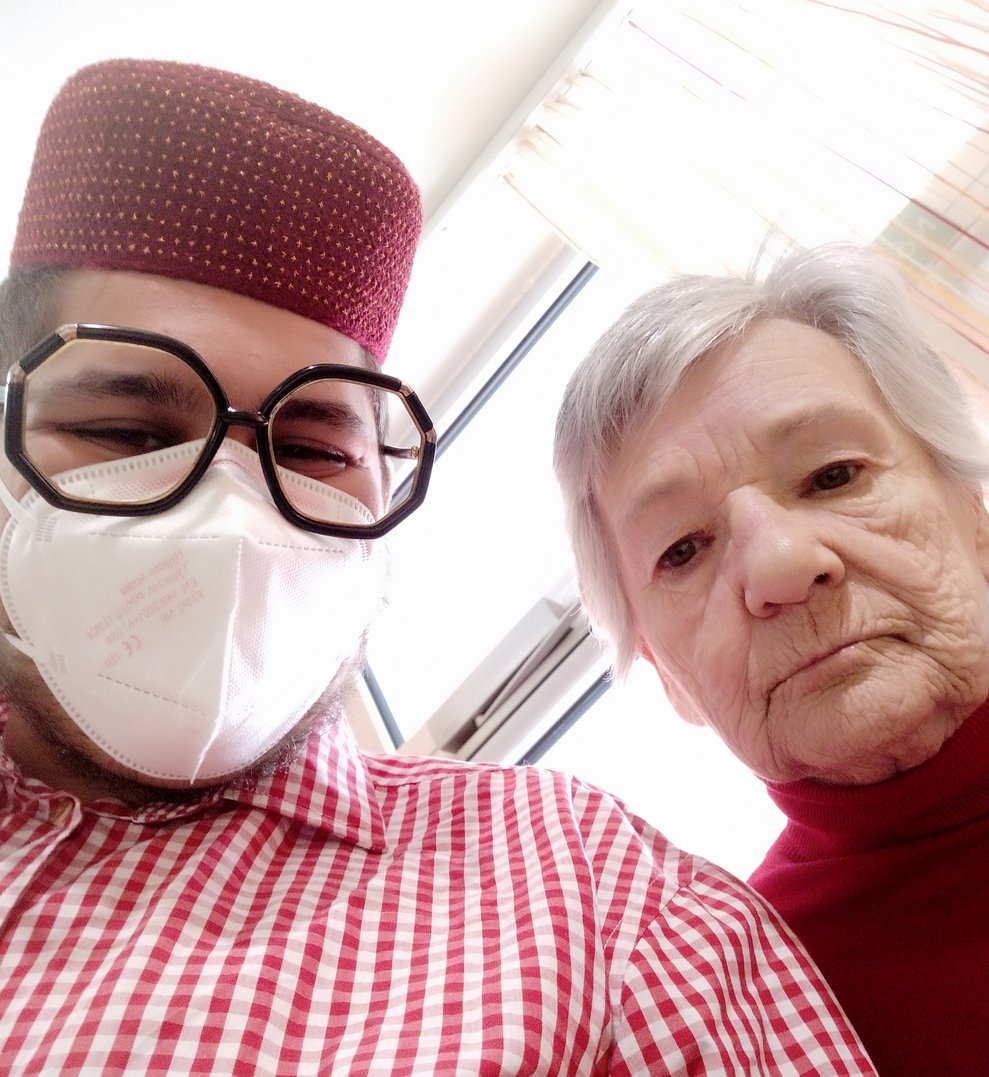 Ein Betreuer mit Brille und kariertem Hemd steht neben einer Bewohnerin.