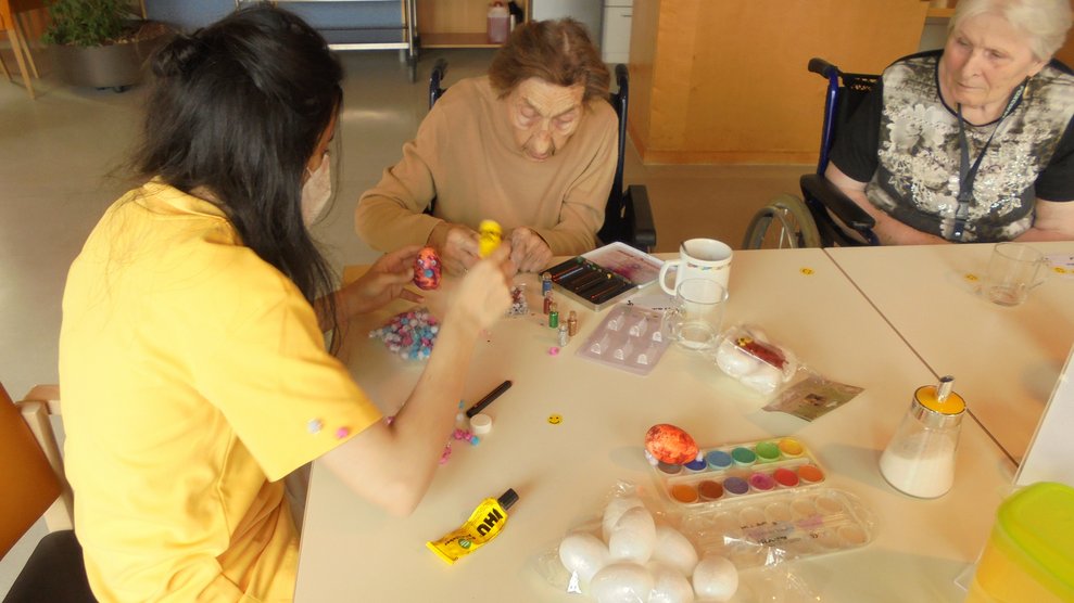 Zwei Bewohnerinnen und eine Betreuerin dekorieren Ostereier.