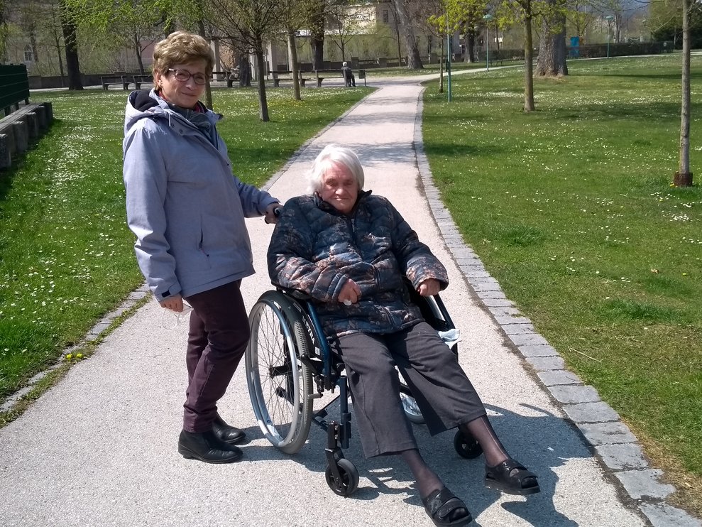 Eine Bewohnerin wird mit dem Rollstuhl durch den Park geschoben.
